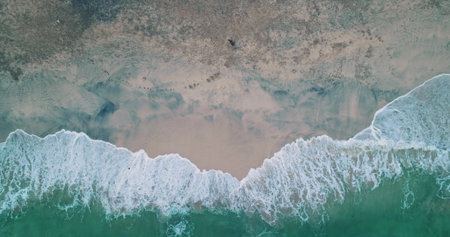 Turquoise ocean waves are rhythmically crashing onto the sandy shore of Bias Tugel Beach in Bali, Indonesia, creating a mesmerizing natural spectacle as seen from an aerial drone perspectiveの写真素材