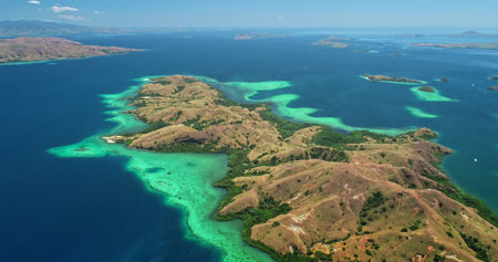 Breathtaking aerial view of Komodo national park in Indonesia, featuring vibrant turquoise waters caressing lush, hilly islands beneath a clear blue skyの写真素材