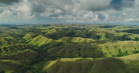 Lush green hills stretch as far as the eye can see across Sumba Island, Indonesia, creating a...