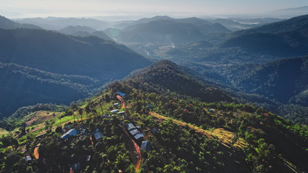 Early morning sunlight illuminating a remote mountain village in Chiang Mai Province, Thailand, reveals the tranquil beauty of lush mountains stretching into the distanceの写真素材
