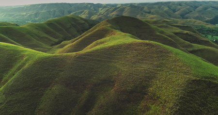 Aerial view of the undulating landscape of Sumba Island, Indonesia, bathed in the warm glow of...