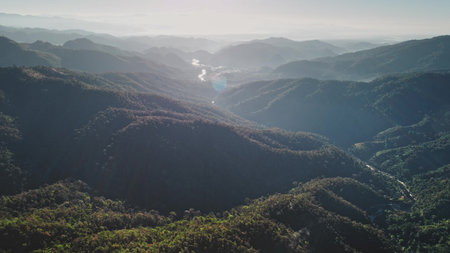 Aerial view of sunlight illuminating forested mountains and a river valley in Chiang Mai Province, Thailand, showcasing the natural beauty and tranquility of Southeast Asiaの写真素材