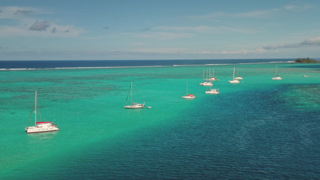 Aerial drone view of sailboats yachts and catamarans moored in shallow, turquoise water near a...