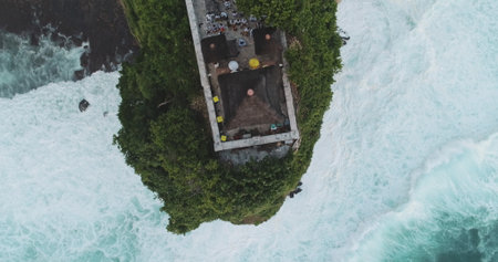 Aerial drone capturing Batu Bolong Temple at high tide, highlighting crashing waves against cliffs while tourists explore the stunning coastal sceneryの写真素材