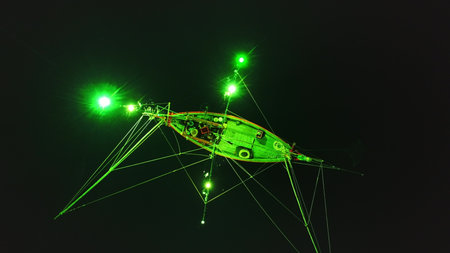 Aerial night view of a traditional Thai squid fishing boat using green lights to attract its prey in...