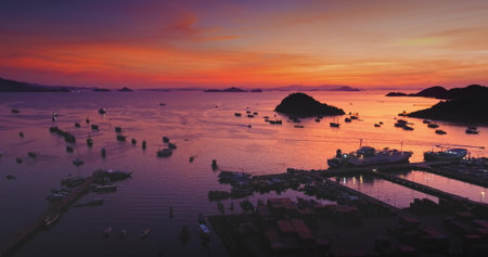 Aerial view of Ende Port in Flores Island, Indonesia, showing boats sailing on the sea during a vibrant and colorful sunset, with islands and mountains in the backgroundの写真素材