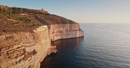 Malta: Golden sunset light reflecting on Dingli rocks cliffs, the highest point of Malta, with the Mediterranean Sea calm waters shining below, aerial drone flightの写真素材