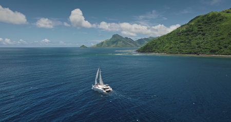 Fiji, Kuata island: White catamaran sailing through calm blue ocean water near green mountains...