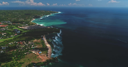 Aerial view of Dreamland Beach meeting the vastness of the Indian Ocean, showcasing the vibrant coastline of Bali, Indonesia, with lush greenery and resorts dotting the landscape under a bright skyの写真素材