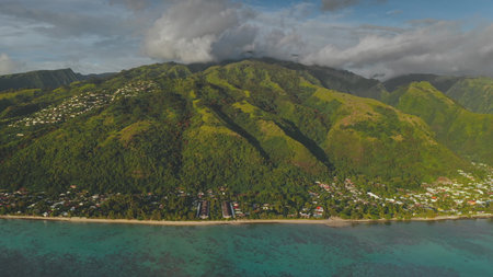 Stunning aerial view of Tahiti island, showcasing its verdant mountains, coastal resorts, and clear turquoise waters under a dramatic cloudscape, capturing the essence of tropical paradiseの写真素材