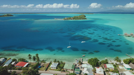 Two sailboats sailing turquoise water near luxury beach resort in Bora Bora, French Polynesia. Lush...