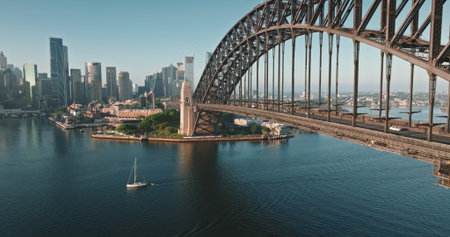 Australia, Sydney: Sydney Harbour Bridge and city skyline, sailboat glides under sunny morning blue sky. Travel destination, modern cityscape architecture in background. Aerial view droneの写真素材