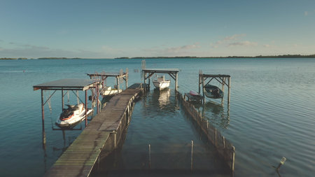 Wooden pier extending into turquoise lagoon, revealing shallow seabed, moored boats, and distant horizon under sunny skies, capturing tropical paradise landscapeの写真素材