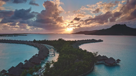 Luxury wooden villas hotel in coral reef lagoon. Exclusive resort overwater bungalows on Bora Bora. Remote romantic honeymoon, exotic summer travel. Aerial drone flight. Amazing colorful sunset skyの写真素材