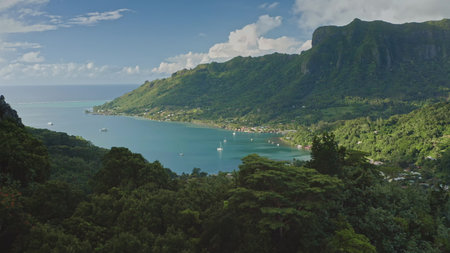 Moorea mountainous landscape with serene sailboats nestled in turquoise lagoon under cloudy blue sky. Opunohu bay, green mountains tropical paradise. Popular tourist destination, exotic summer travelの写真素材
