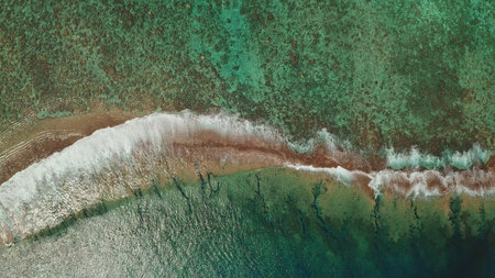 Stunning aerial top down drone captures breathtaking beauty of powerful ocean waves crashing vibrant coral reef barrier turquoise water. Remote wild nature. Natural background. Static shotの写真素材