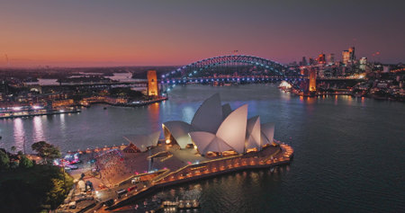 Australia, Sydney: aerial view of Sydney Opera House and Harbour Bridge illuminated at sunset, vibrant colorful evening sky over modern cityscape and harbor. Travel destination. Drone flightの写真素材