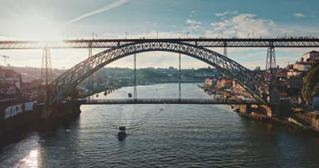 Portugal, Porto: Dom Luis I Bridge spanning Douro River at sunset, modern buildings along the riverbank and a boat gliding below, showcasing urban city landscape. Aerial view drone zoom outの写真素材