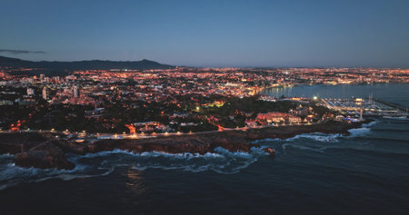 Breathtaking aerial view of Cascais at dusk, highlighting the illuminated cityscape along the coastline, with gentle Atlantic waves contrasting land and sea. Droneの写真素材