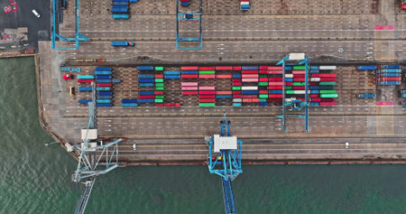 Busy industrial shipping ocean port with colorful freight cargo containers stacked, forming the word LOGISTICS, with gantry cranes and trucks moving along the dock. Aerial drone top down viewの写真素材