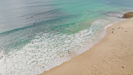 Aerial drone view shows surfers and people enjoying the turquoise water and sandy beach, with gentle...