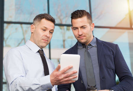 Two businessmen using touchpad together outdoorsの写真素材