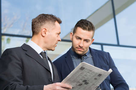 Two serious businessmen reading newspapers togetherの写真素材