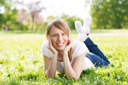 Smiling woman lying in grass and enjoying in nature. She is looking at the cameraの写真素材