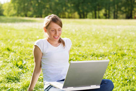 Smiling woman sitting among  grass and using laptop computerの写真素材
