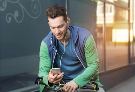 Young man in city checking his smart phone while sitting on a bicycleの写真素材