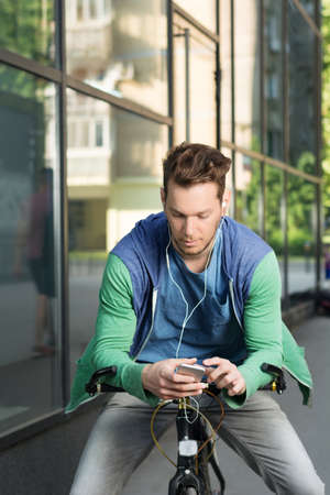 Young man in city checking his smart phone while sitting on a bicycleの写真素材