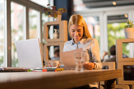 Young smiling businesswoman using laptop in the office while reading documents.の写真素材