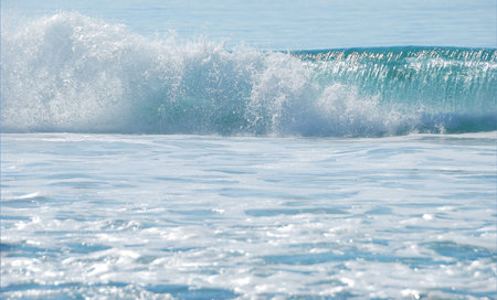 breaking ocean wave shown on a sunny day with foam in the foreground