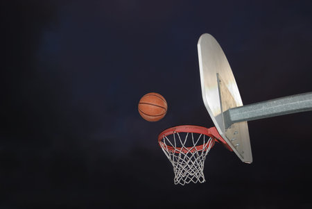 Basketball going into the hoop at an outdoor court in the darkの写真素材