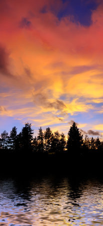 red clouds at sunset above tree silhouettes reflecting in the water on the Lake Tahoe Californiaの写真素材
