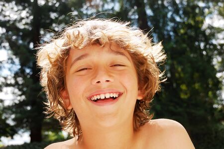 Smiling teen boy enjoying summer against blurry tree and sky background.の写真素材