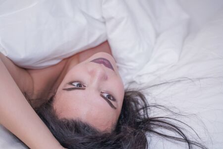 charming young brunette girl resting in her white bedの写真素材