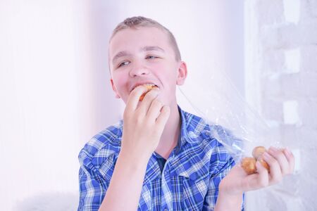 cute hungry teenager boy with fresh small bake sweets on white room background aloneの写真素材