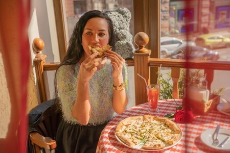 Funny brunette girl in sweater eating pizza at restaurant.の写真素材