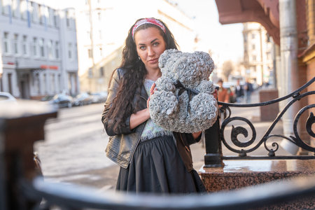 pretty cheerful happy adult girl with grey teddy bear from roses in the cityの写真素材
