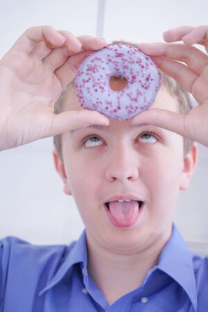 Little happy cute boy is eating donut on white kitchen background aloneの写真素材