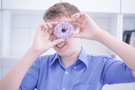 Little happy cute boy is eating donut on white kitchen background aloneの写真素材