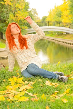 Beautiful young redhead woman in sweater walks in autumnの写真素材