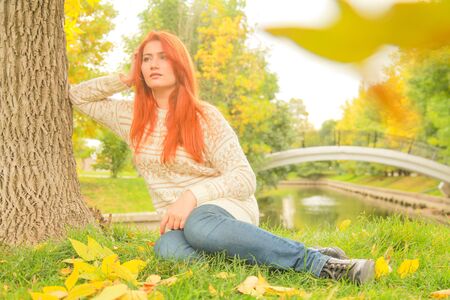 Beautiful young redhead woman in sweater walks in autumnの写真素材