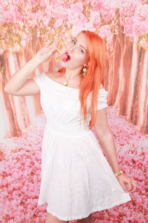 Surprised sexy girl eating lollipop. Beauty Glamour Model woman with orange hair holding pink candyの写真素材