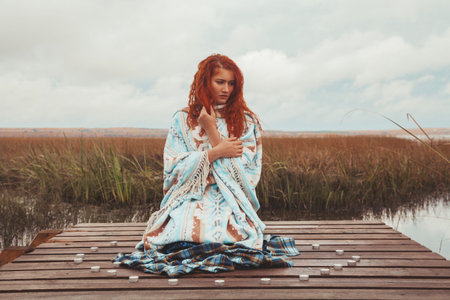 woman practices yoga and meditates with many candles near the autumn lakeの写真素材