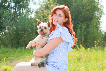 Cheerful pretty young woman sitting and hugging her dog on the natureの写真素材