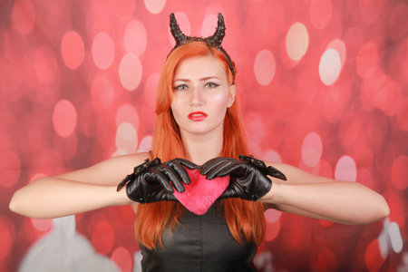 Devil girl with pink plush toy with heart shape on red background