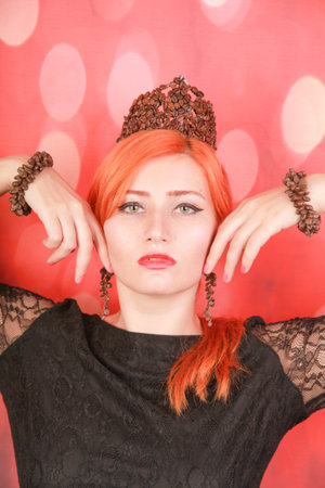 Woman enjoying tasty aroma of coffee and wear crown with coffee beans on red christmas backgroundの写真素材