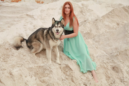 Funny best friends concept. Happy young female person walks in the desert with big dog malamute outdoorsの写真素材
